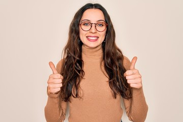 Wall Mural - Young beautiful woman wearing casual turtleneck sweater and glasses over white background success sign doing positive gesture with hand, thumbs up smiling and happy. Cheerful expression and winner