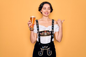 Wall Mural - Young beautiful german woman with blue eyes wearing octoberfest dress drinking glass of beer pointing and showing with thumb up to the side with happy face smiling