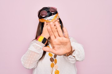 Sticker - Young hispanic hippie woman wearing fashion boho style and sunglasses over pink background covering eyes with hands and doing stop gesture with sad and fear expression. Embarrassed and negative