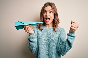 Young blonde girl holding paper plane as success on business and communication screaming proud and celebrating victory and success very excited, cheering emotion