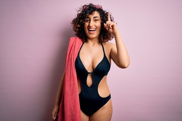 Sticker - Young beautiful curly arab woman on vacation wearing swimsuit holding beach towel surprised with an idea or question pointing finger with happy face, number one