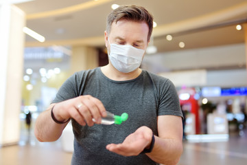 Man wearing disposable medical face mask makes disinfection of hands with sanitizer in airport, supermarket or other public place. Safety during coronavirus outbreak.