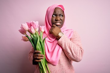 Poster - Young african american plus size woman wearing muslim hijab holding bouquet of pink tulips Thinking worried about a question, concerned and nervous with hand on chin