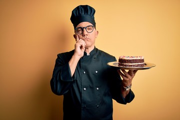 Sticker - Middle age handsome grey-haired baker man wearing cooker uniform and hat holding cake serious face thinking about question, very confused idea