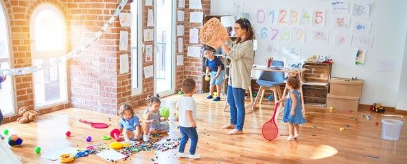 beautiful teacher and group of toddlers playing around lots of toys at kindergarten