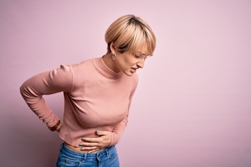 Poster - Young blonde woman with short hair wearing casual turtleneck sweater over pink background Suffering of backache, touching back with hand, muscular pain