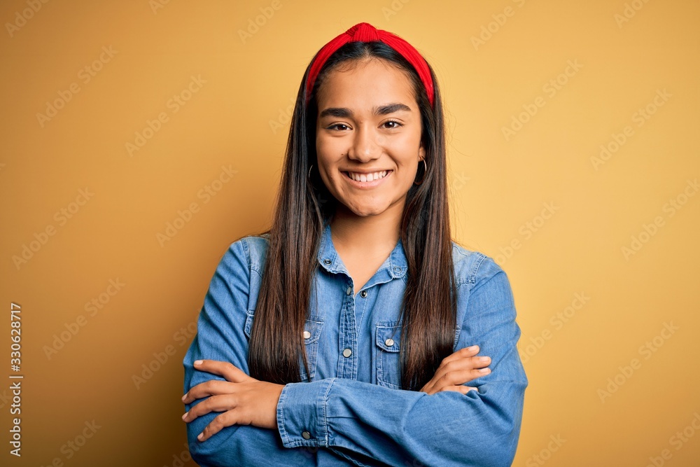 Young beautiful asian woman wearing casual denim shirt and diadem over yellow background happy face smiling with crossed arms looking at the camera. Positive person. - obrazy, fototapety, plakaty 