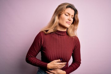 Canvas Print - Young beautiful blonde woman wearing casual sweater over isolated pink background with hand on stomach because indigestion, painful illness feeling unwell. Ache concept.