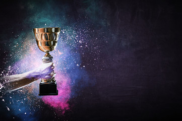 Hand holding up a gold trophy cup against dark background