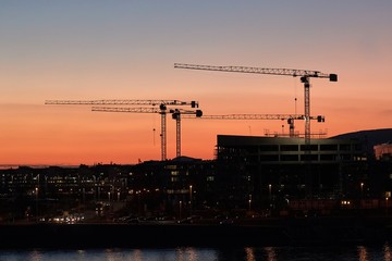 Construction cranes against dramatic twilight red glow sky