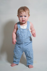 Wall Mural -  emotional portrait of a one-year-old baby in denim overalls on a uniform light background