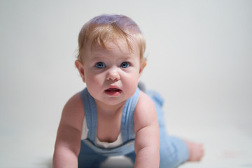 Wall Mural -  emotional portrait of a one-year-old baby in denim overalls on a uniform light background