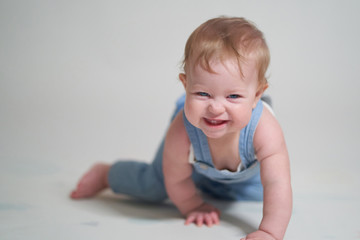 Wall Mural -  emotional portrait of a one-year-old baby in denim overalls on a uniform light background