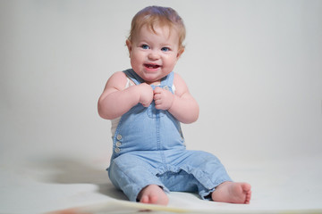 Wall Mural -  emotional portrait of a one-year-old baby in denim overalls on a uniform light background