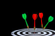 © sirastock - Red and green dart arrow hitting target center is Dart board Isolated on black background