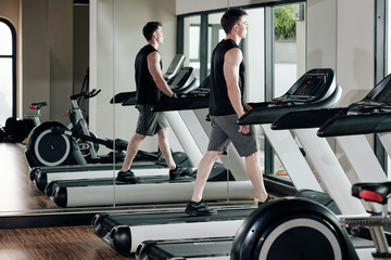 Young fit pensive sportsman walking on treadmill and warming up before training