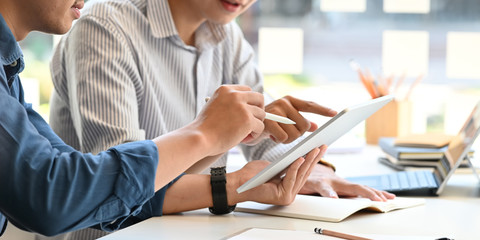 Photo of young business development team discussing/talking/explaining about their business plan by using a computer tablet and stylus pen while sitting at the modern working table in orderly office.