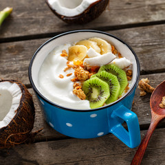 Wall Mural - Tasty and healthy breakfast. Bowl fruit coconut yogurt with granola on wooden table. Healthy vegan food concept