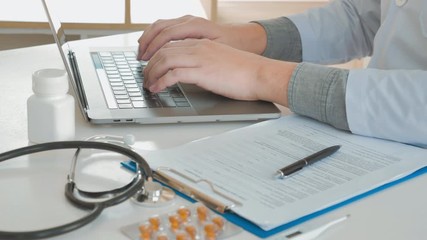 Wall Mural - Doctor typing information on Laptop in Hospital office focus on Stethoscope