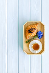 Poster - Breakfast with summer flowers. Tea, croissant and cornflowers on blue wooden background top-down copy space