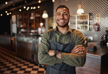 Afro-american cafe owner standing smiling wearing apron with folded arms