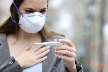 Woman with protective mask checking thermometer