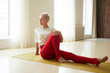 © shurkin_son - Beautiful mature woman with gray pixie hair and athletic body sitting on mat turning torso to side with one knee bent, doing stretching exercises during morning yoga, having energetic look