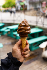 Wall Mural - Man holding dipped chocolate ice cream cone in hand, very blurred background, small depth of field. Dark background.