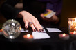Fortuneteller's hands with cards at table with candles, magic ball in dark room