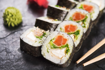 Canvas Print - Closeup of sushi roll with salmon on a black slate background. japanese food menu