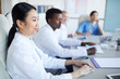© Seventyfour - Side view at multi-ethnic group of doctors sitting at table during medical conference, focus on smiling Asian woman in foreground, copy space