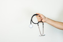 Male Hand Holds A Stethoscope On A Light Isolated Background. Concept Medicine, First Aid, Medical Education, Intern. Banner