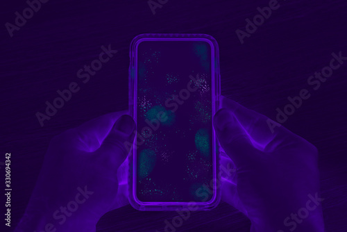 Hands holding cell phone with dirty contaminated touch screen - UV Blacklight exposing infectious bacteria and harmful germs on mobile smartphone display -  Disease, corona virus and hygiene concept