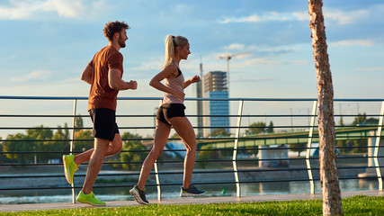 Modern woman and man jogging / exercising in urban surroundings near the river.