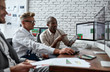 © Svitlana - Ideas ahead. Successful businessmen trading stocks. Stock traders looking at graphs, indexes and numbers on multiple computer screens. Three colleagues in modern office