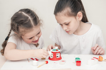 Two girls, an older sister and a younger one, make a house out of clay and decorate it