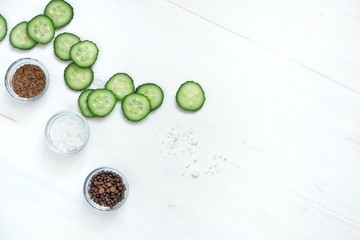 Wall Mural - Sliced cucumber slices, salt, pepper, spices in glass bowls on a white wooden table. Freshness concept, vegetarianism, salad ingredients. Top view, flat lay, copy space for text.