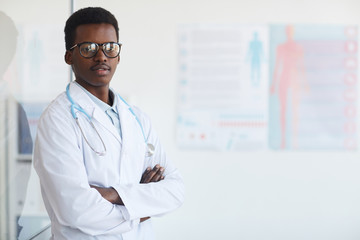 Wall Mural - Waist up portrait of young African-American doctor standing with arms crossed while posing in med clinic, copy space