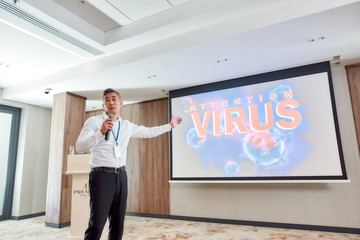 Wall Mural - Attention. Asian male speaker in suit with headset and laser pointer giving a talk at corporate business meeting with the theme of coronavirus