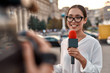 © Svitlana - Watch us work for you. TV reporter presenting the news outdoors. Journalism industry, live streaming concept.