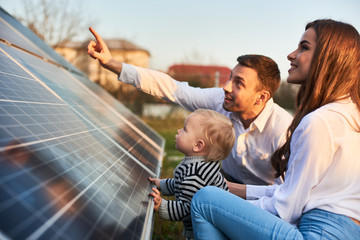 man shows his family the solar panels on the plot near the house during a warm day. young woman with