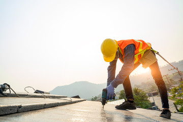 Poster - Roofer worker in protective uniform wear and gloves,Using air or pneumatic nail gun and installing concrete roof tile on top of the new roof,Concept of residential building under construction.