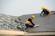 © visoot - Roofer worker in special protective work wear and gloves,Using pneumatic gun and installing concrete roof tile on top of the new roof,Concept of residential building under construction.