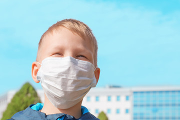 European cute boy in a protective medical mask outdoor on a clear sunny day. Virus disease prevention, virus protection concept.