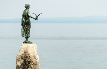 Maiden girl holding a seagull and facing the sea, statue on rocks, Opatija