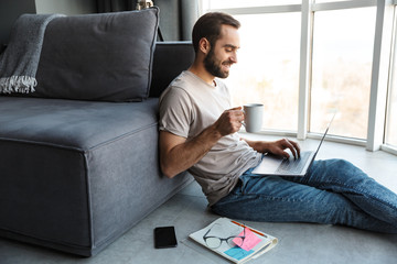 Wall Mural - Attractive smart young man sitting on a floor in the living room