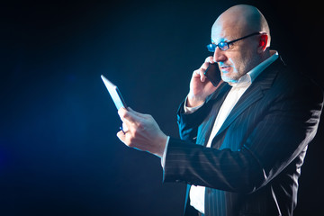 Poster - The man is holding an electronic tablet and talking on a mobile phone. A businessman uses computer gadgets in his work. Discussion of the details of the new contract.