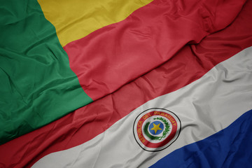 waving colorful flag of paraguay and national flag of benin.