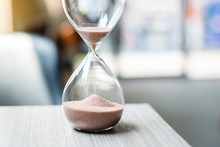 Hourglass On Table Office With Copy Space, Sand Flowing Through The Bulb Of Sandglass Measuring The Passing Time. Countdown, Deadline, Life Time And Retirement Concept