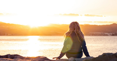 inspiration wallpaper picture of lonely girl sitting back to camera on Red sea bay Gulf of Aqaba Middle East region Eilat city coast line in vivid bright sunset time with sun glares